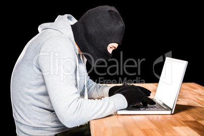 Focused thief with hood typing on laptop