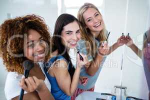 Three smiling friends putting makeup on together