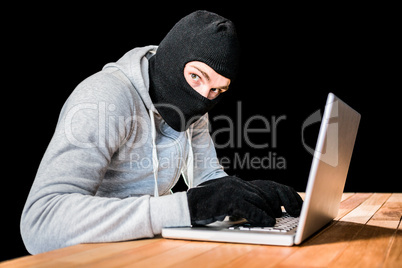 Focused thief with hood typing on laptop