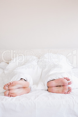 Bare feet of gay couple out from the blanket