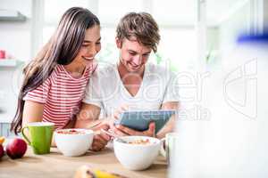 Happy couple using tablet and having breakfast