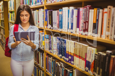 Brunette student using her tablet next to bookshelves