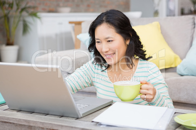 Smiling brunette using laptop and holding mug