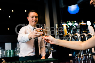 Smiling barman giving glass of white wine to client