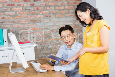 Smiling pregnant woman showing tablet to her husband