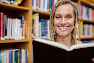 Happy female student reading a book in the library