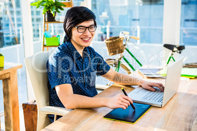 Smiling hipster businessman using laptop and graphic tablet