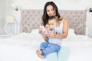 Happy brunette holding her baby and using smartphone