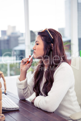 Focused Asian woman with pen on chin