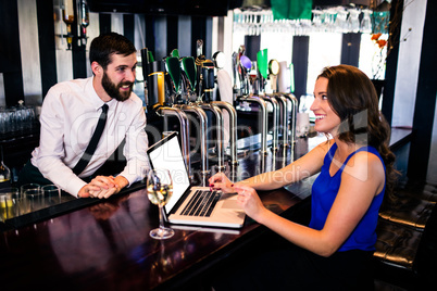 Barman talking to customer using laptop