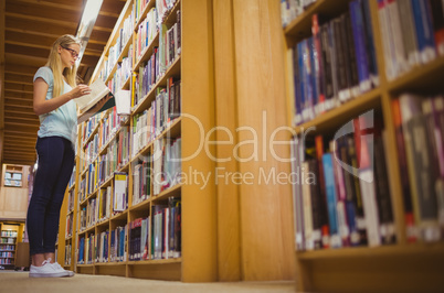 Blonde student reading book next to bookshelf