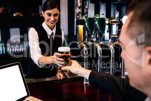 Barmaid serving a pint to customer with laptop