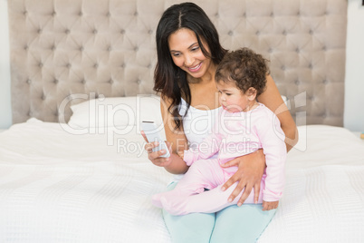 Smiling brunette holding her baby and using smartphone