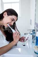 Brunette using smartphone while brushing teeth