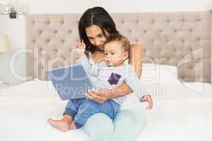 Happy brunette holding her baby and using tablet