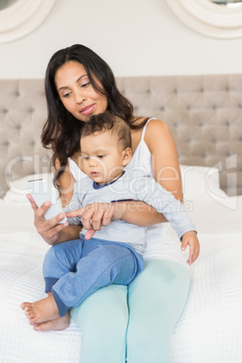 Happy brunette holding her baby and using smartphone