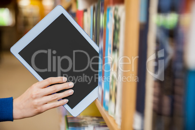 Female student tidying a tablet in a bookshelf