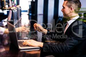 Businessman getting a glass of wine and using laptop