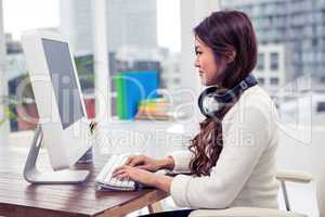 Asian woman using computer with headphones around neck