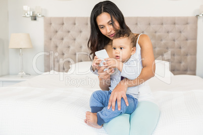 Happy brunette holding her baby and using smartphone
