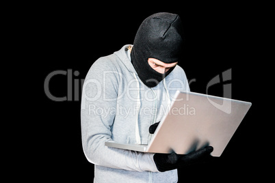 Focused thief with hood typing on laptop