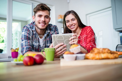 Happy couple having breakfast and using tablet