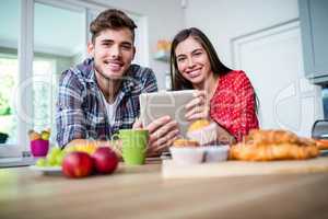 Happy couple having breakfast and using tablet