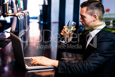 Businessman getting a glass of wine and using laptop