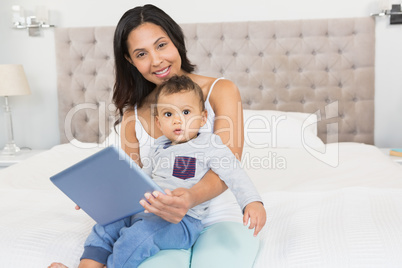 Happy brunette holding her baby and using tablet