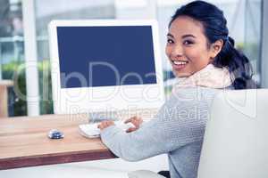 Smiling Asian woman using computer looking back at the camera