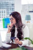 Asian woman with hand on chin holding credit card