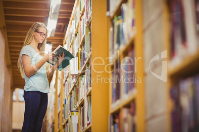 Blonde student reading book next to bookshelf