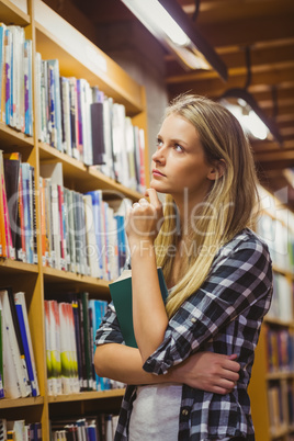 Thoughtful student looking at bookshelf