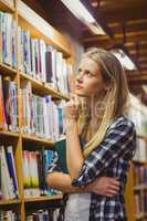 Thoughtful student looking at bookshelf