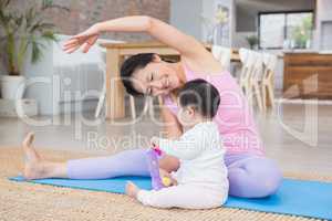 Happy mother doing yoga on mat while looking at baby daughter