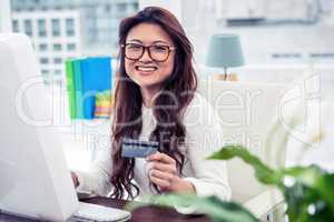 Smiling Asian woman on computer holding credit card