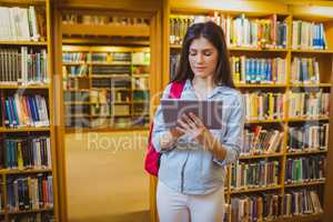 Brunette student using her tablet next to bookshelves