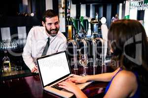 Barman talking to customer using laptop