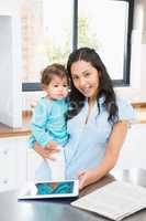 Smiling brunette holding her baby and using tablet