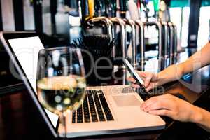 Woman texting and using laptop with wine