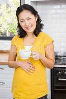 Smiling pregnant woman holding mug and touching her belly
