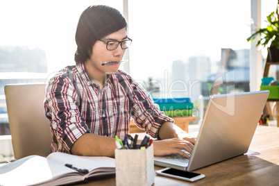 Hipster businessman with pen in mouth using laptop