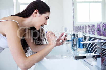 Brunette using smartphone while brushing teeth