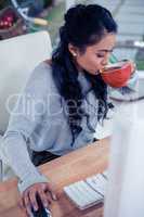 Pretty Asian woman using computer and drinking by cup