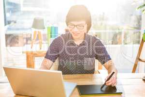 Smiling hipster businessman using laptop and graphic tablet