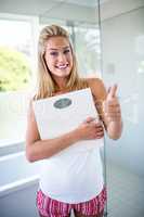 Woman holding a weighting scale with thumbs up