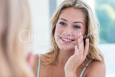 Smiling pretty woman applying cream on her face