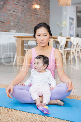 Serious woman sitting on mat with baby daughter