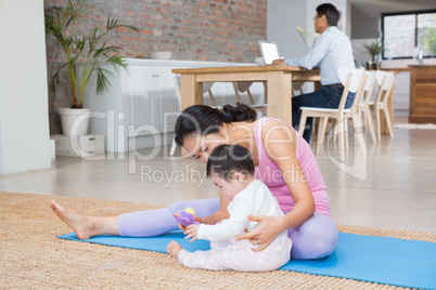Happy mother and baby daughter sitting on exercising mat