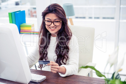 Smiling Asian woman on computer holding credit card